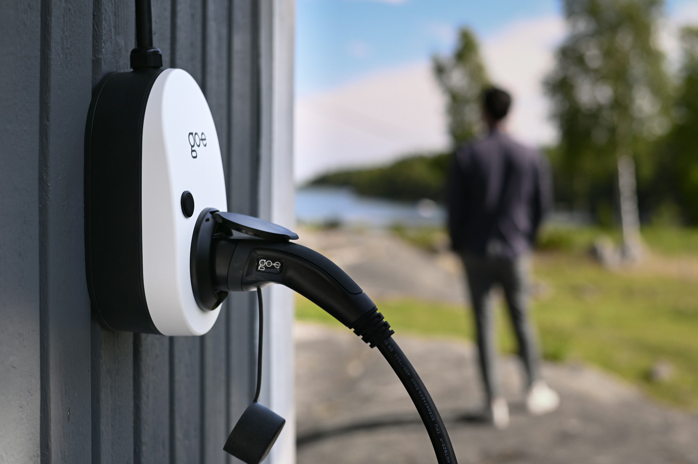 Borne de recharge murale en extérieur, câble branché, scène lumineuse en bord de lac